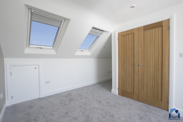 Simple bedroom with double Velux windows featuring almost-open Velux blackout blinds with blue sky beyond