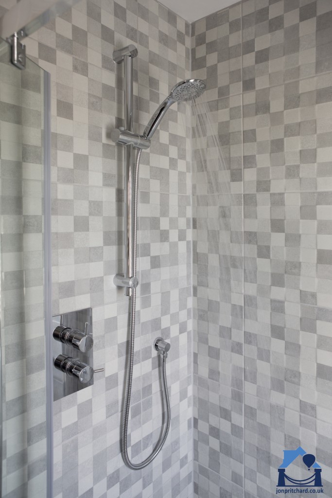 Portriat orientation photo of a modern tiled shower enclosure in attractive grey 'large' mosaic matt tiles. The water is running, shower is facing right.