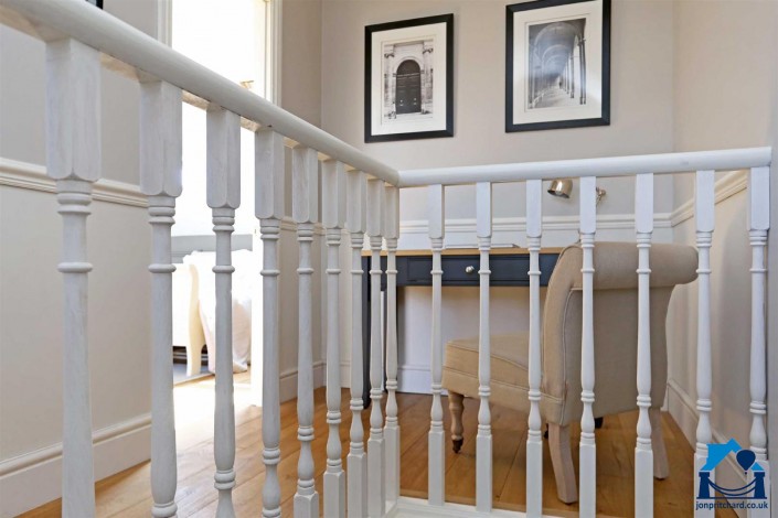 Photo showing a small landing study space in a stylish loft conversion featuring traditional staircase spindles painted white.