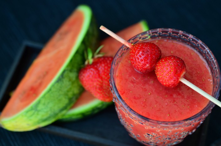 Image of a watermelon and strawberry cocktail from above, with strawberries on a stick over the glass and slices of watermelon in the background