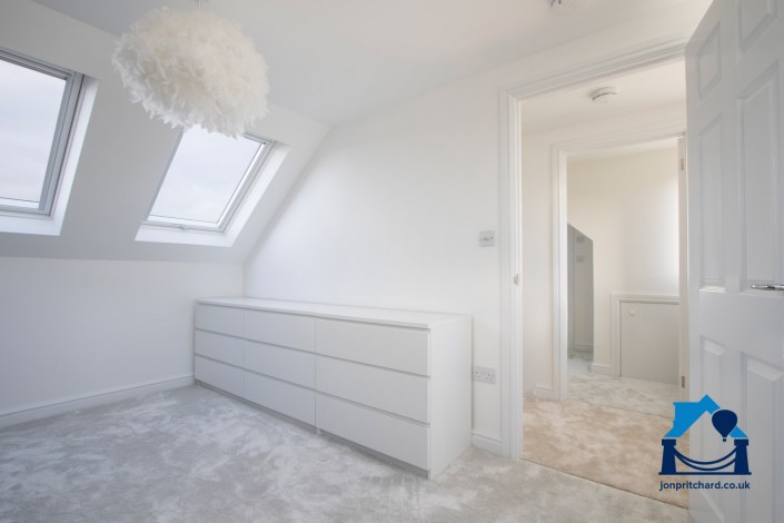 Landscape orientation photo showing the room flow of a loft conversion, from double bedroom through the door to a small landing, and dressing room/ensuite beyond