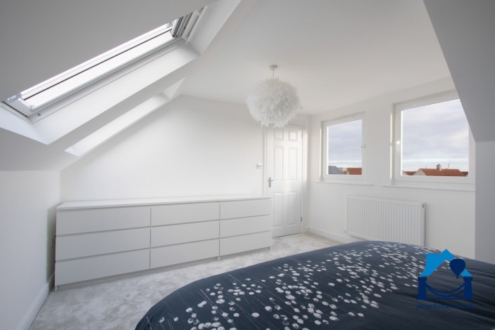 Interior image of a loft conversion bedroom, showing vertical windows in a flat roofed dormer, overlooking the neighbourhood.