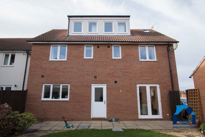 Image of rear of a new build detached home, with a loft conversion that includes an attractive long flat-roofed dormer.