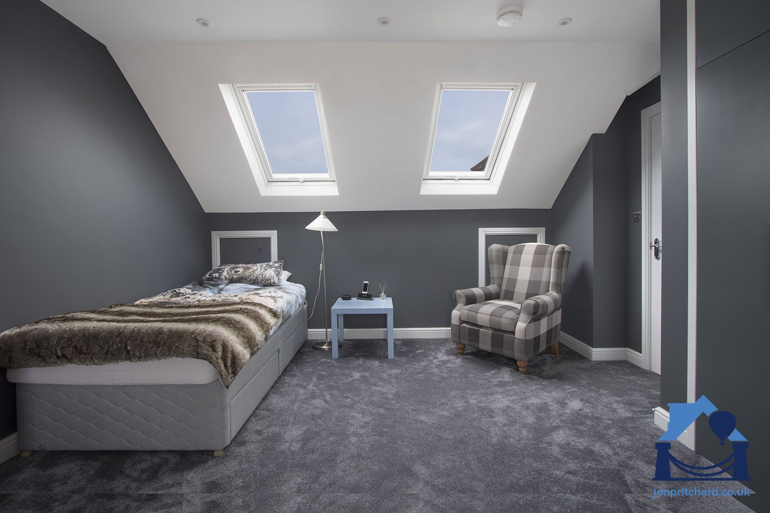 Photo showing a stylish loft conversion bedroom with single bed, armchair, fitted wardrobes and two VELUX windows